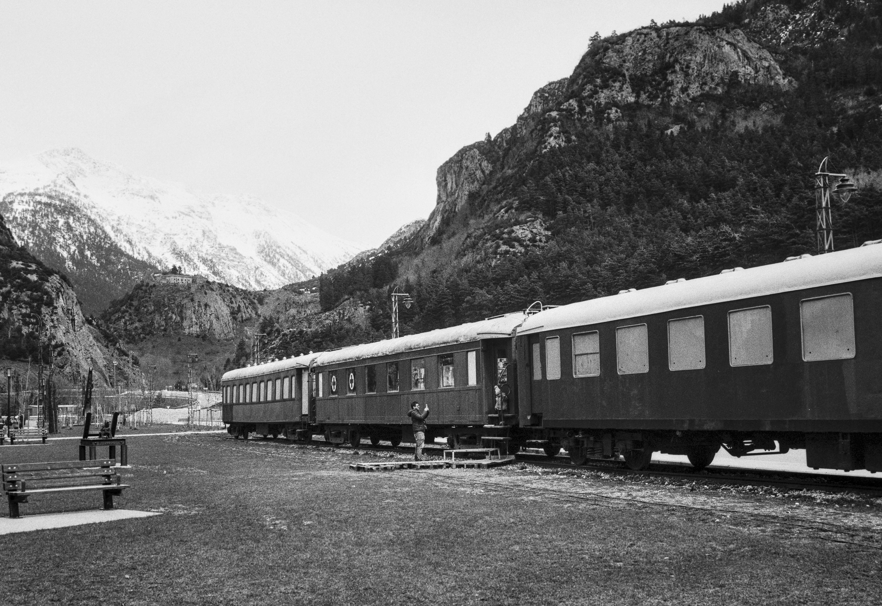A father lifts his child onto the steps of an old train carriage in Canfranc, with snow-covered Pyrenees rising in the background.