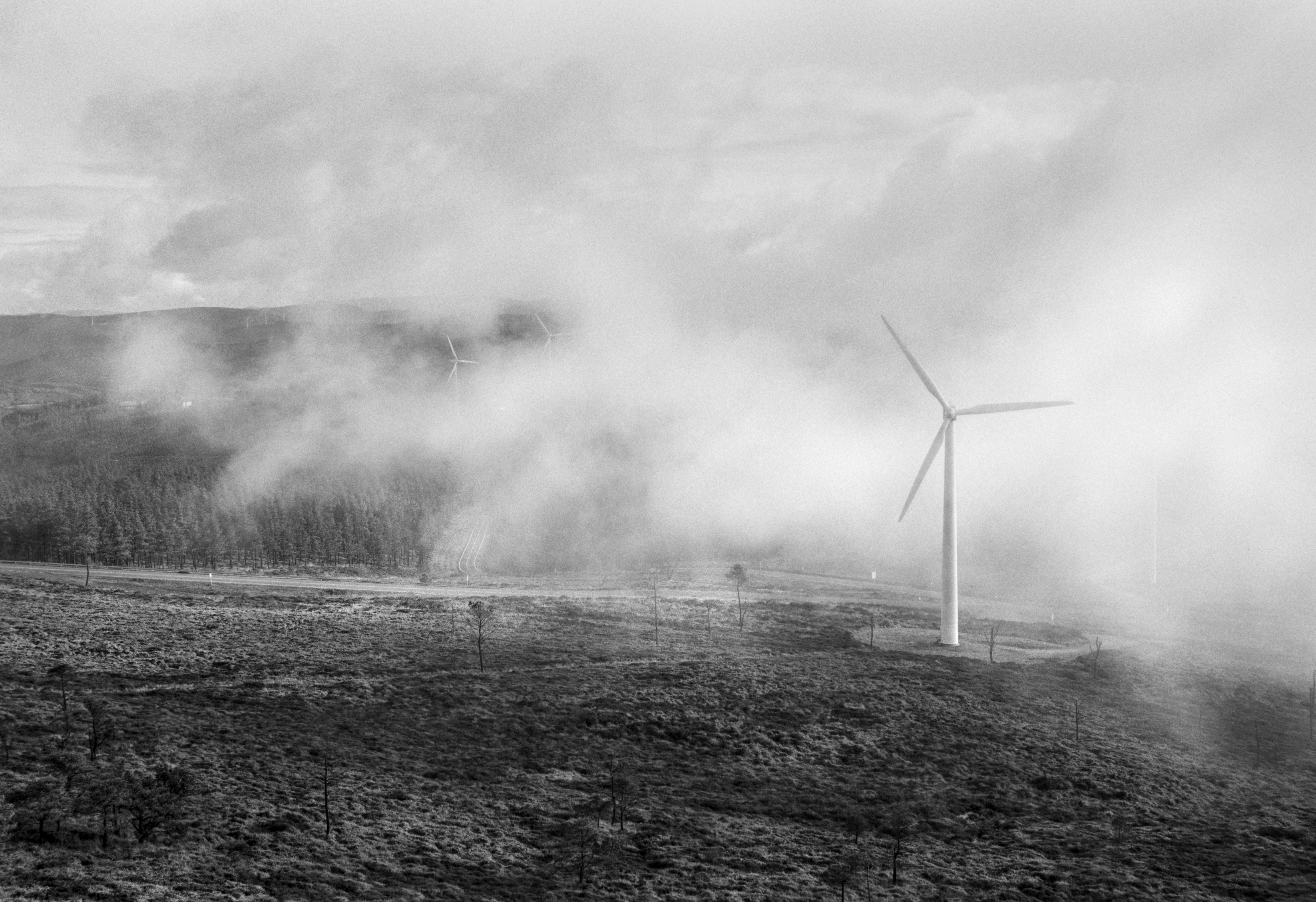 Mist drifting across Mount Caxado, partially revealing wind turbines rising above the landscape.