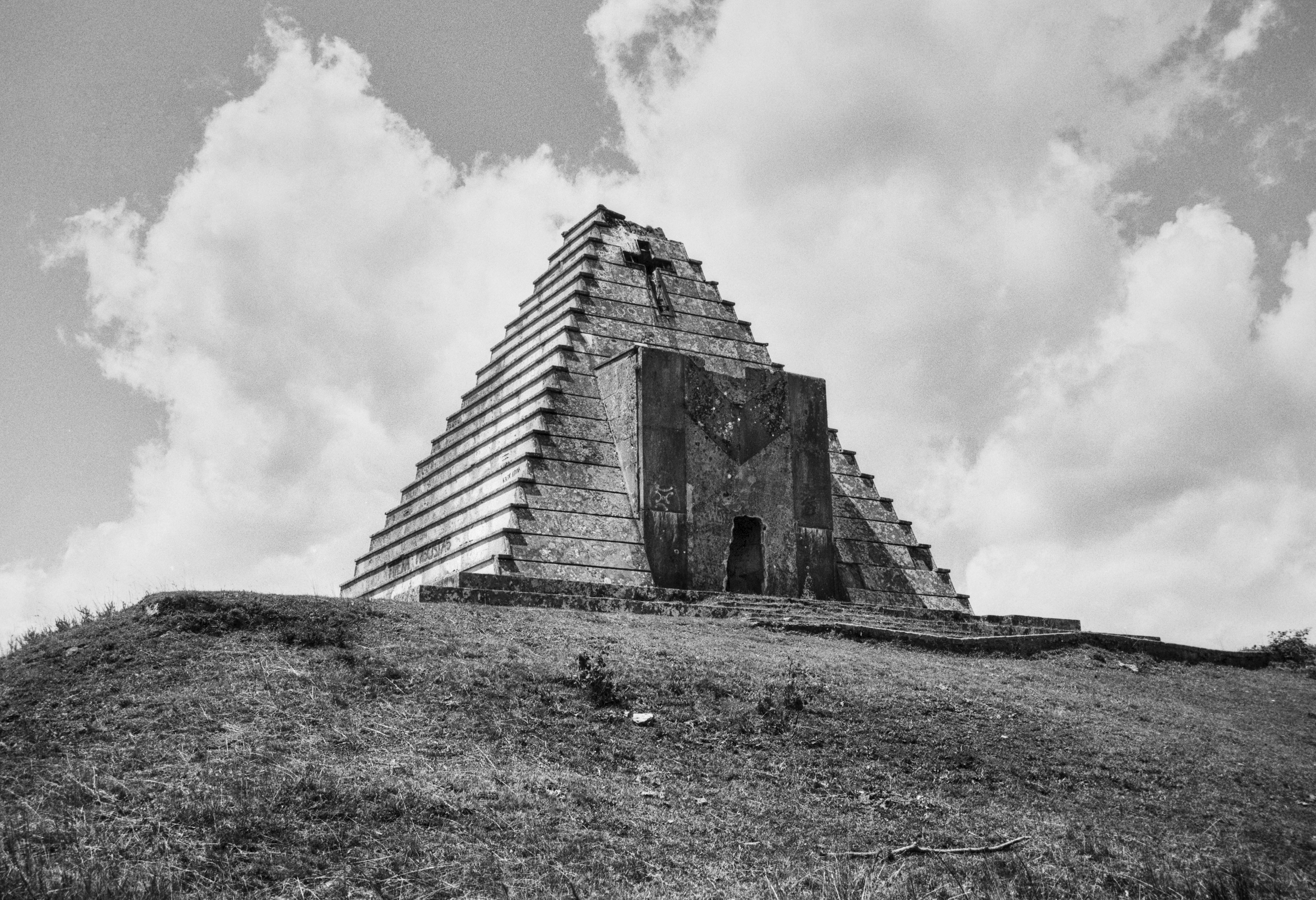 Abandoned pyramid-shaped mausoleum known as La Pirámide de los Italianos, standing on a hill under a cloudy sky.