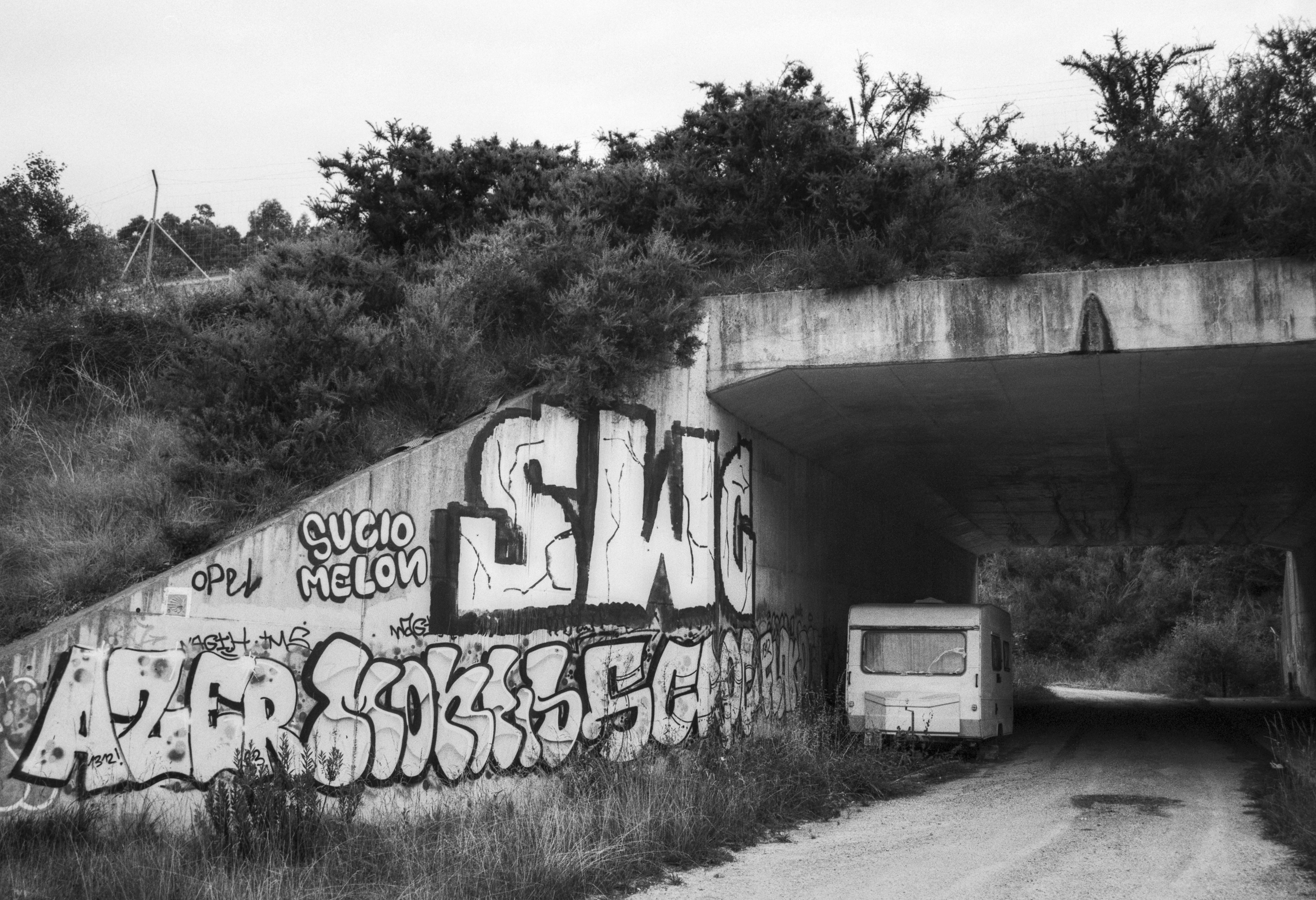Abandoned caravan parked under a graffiti covered concrete bridge.