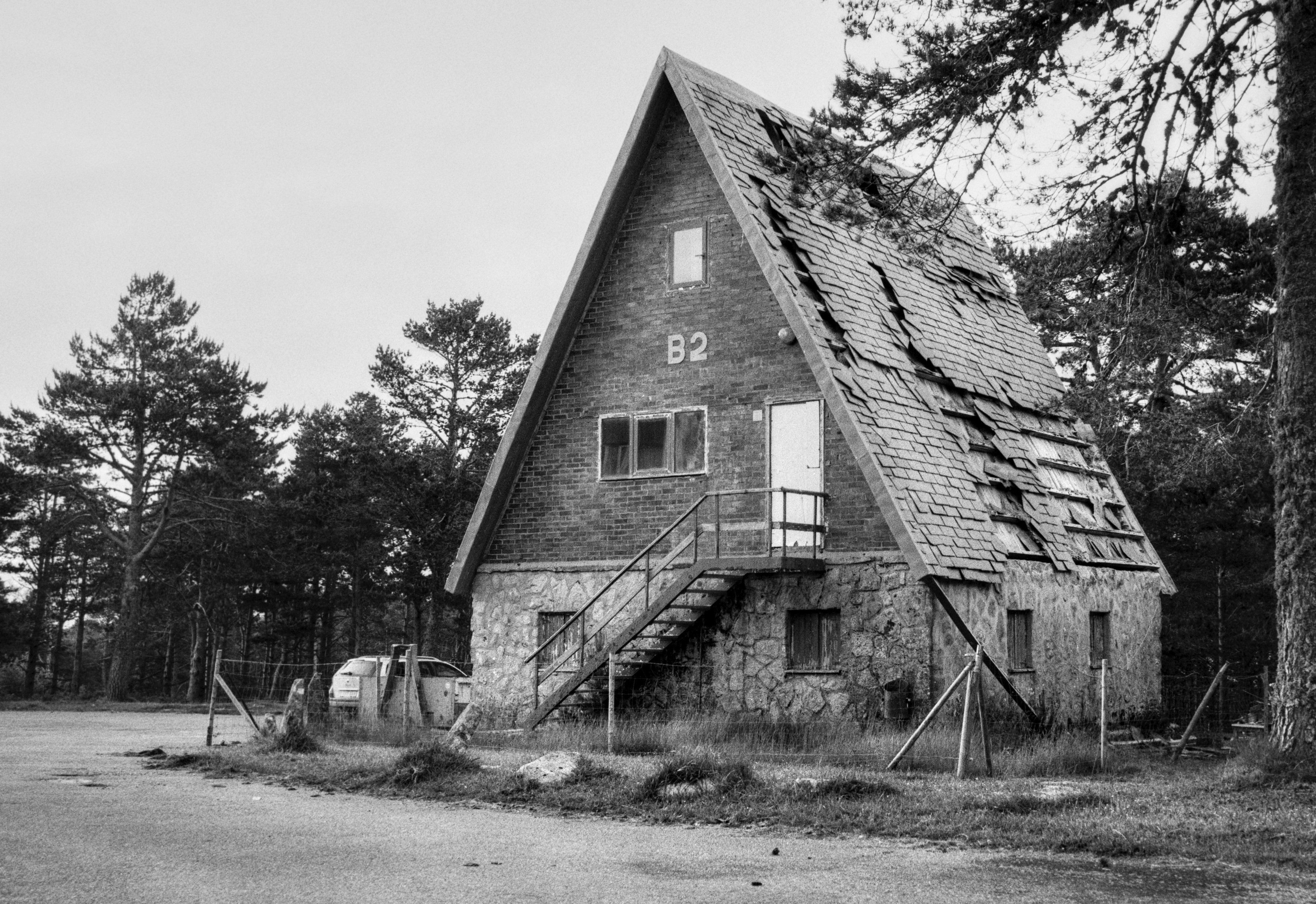 Abandoned wooden bungalows stand among trees at a mountain resort, showing simple structures surrounded by vegetation and an empty, quiet setting.